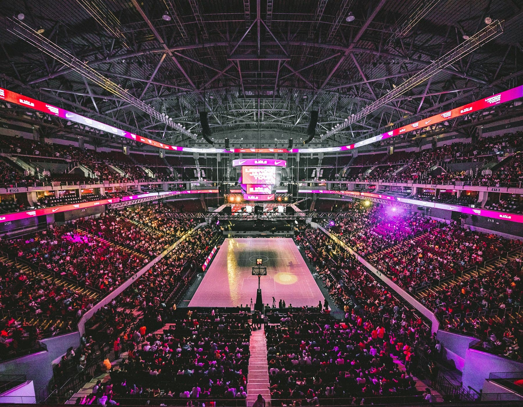A packed basketball arena seen from above, lights low over the court.