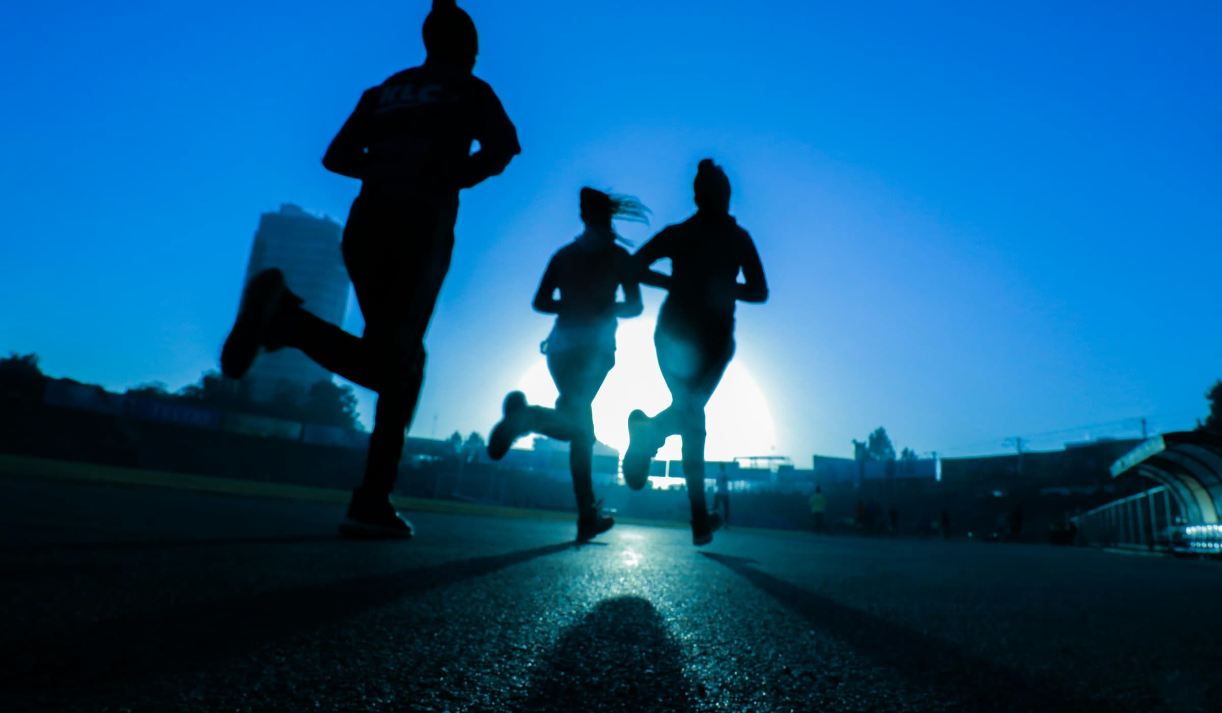 Three athletes running toward a low sun.